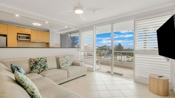 A modern living room with a beige sofa, a ceiling fan, and a view of a balcony with a railing. - Rainbow Place Unit 5- Right on the beach in Rainbow Bay Coolangatta (Coolangatta)