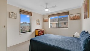 Un dormitorio con una cama, dos ventanas, un ventilador de techo y un aparador.