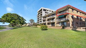 Un edificio residencial de varios pisos con balcones, un césped y un árbol.