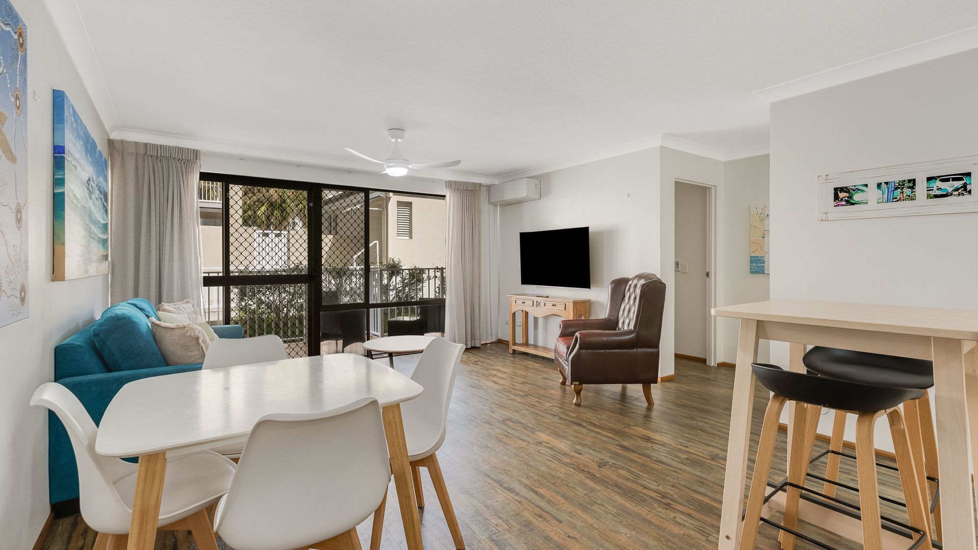 A modern living room with a dining area, a TV, and a balcony with a view.