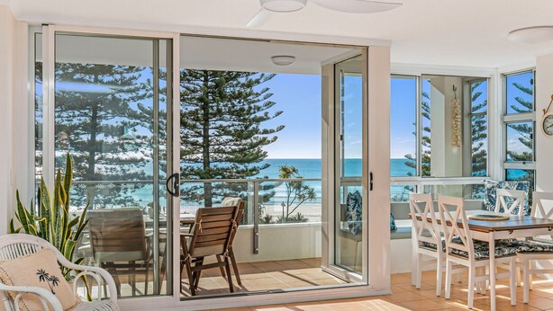 A balcony with a glass door, a dining table with chairs, and a view of the ocean and trees. - Rainbow Pacific Unit 8- Ocean views over Rainbow Bay Coolangatta with free Wi-Fi (Coolangatta)