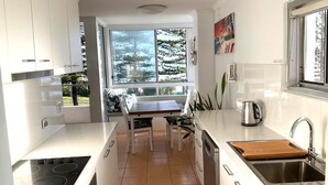 A modern kitchen with white cabinets, a wooden table, and a window with a view of trees. - Rainbow Pacific Unit 8- Ocean views over Rainbow Bay Coolangatta with free Wi-Fi (Coolangatta)