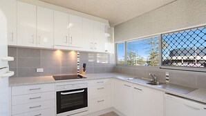 A modern kitchen with white cabinets, a built-in oven, a sink, and a window with a view of trees and buildings. - Kooringal Unit 3 Right on Greenmount Beach Coolangatta with Wi-Fi Included (Coolangatta)