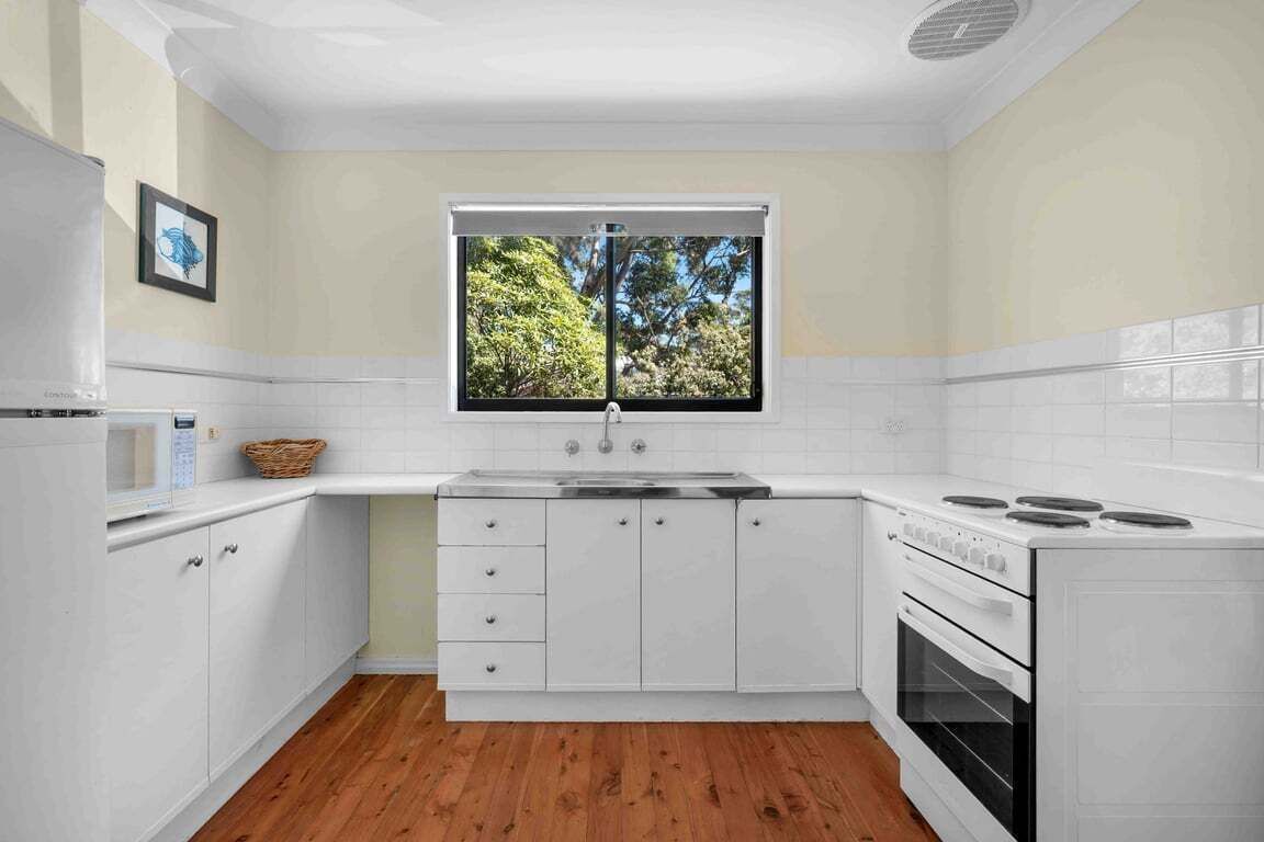 A modern kitchen with white cabinetry, a built-in oven, and a window with a view of trees.