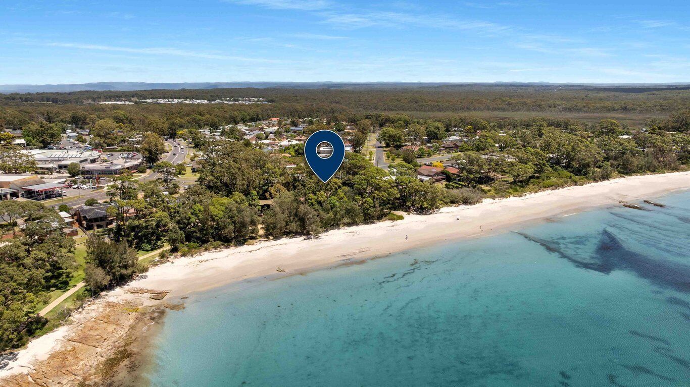 An aerial view of a coastal area with a beach, a small town, and a dense forest.