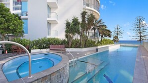 Et moderne poolområde ved hotellet med krystalklart havudsigt, omgivet af frodig vegetation og en hvid bygning med balkoner.