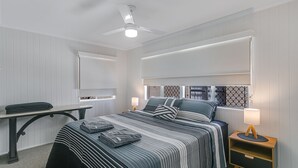 Une chambre à coucher comprenant un lit, des tables de chevet, un bureau et un ventilateur de plafond.