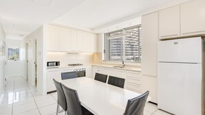 Une cuisine moderne avec des meubles blancs, une table à manger avec des chaises, un réfrigérateur et une fenêtre donnant sur la ville.