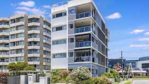 Un immeuble résidentiel moderne à plusieurs étages, doté de balcons, d’une entrée sécurisée et surplombant un ciel dégagé.