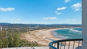Vista costera con playa, edificios y colinas al fondo.