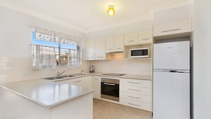 A modern kitchen with white cabinets, a stainless steel sink, a microwave, a built-in oven, and a refrigerator. - Allamanda Court Unit 6 neat and tidy unit handy to Tweed Heads Bowls Club (Tweed Heads)