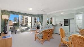 Een modern appartement met balkon, rieten meubilair, een keuken met witte kasten en uitzicht op gebouwen en bomen.
