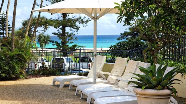 A beachside lounge with white lounge chairs and a large umbrella, overlooking the ocean. - Calypso Plaza Resort Unit 417 Two bedroom unit in resort style complex central Coolangatta (Coolangatta)