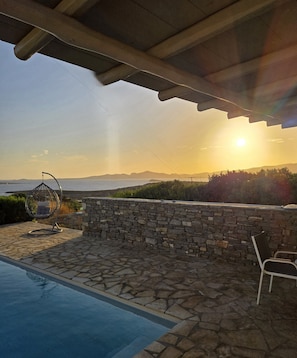 A stone pool with a stone wall and a hanging chair, overlooking a scenic view of the sea and mountains during sunset. - Paros Afrodite Luxury Villas ,Private Pool ,Quiet, Charming & Fantastic View (Paros)