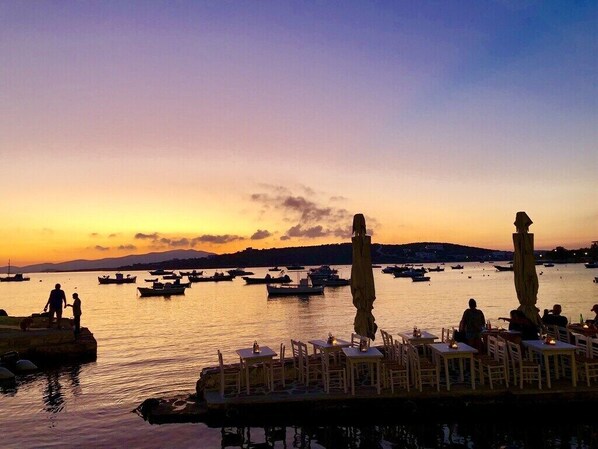 A waterfront restaurant with outdoor seating overlooking the sea, boats in the background, and a sunset sky. - Paros Afrodite Luxury Villas ,Private Pool ,Quiet, Charming & Fantastic View (Paros)