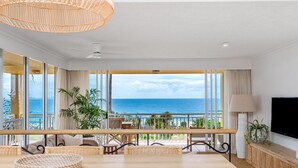 Un balcón amplio con vista al océano, amoblado con mobiliario de mimbre y una mesa de comedor.