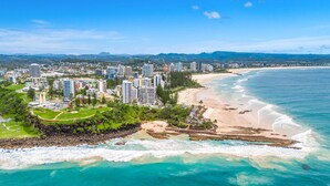 Un paisaje urbano costero con rascacielos, una playa arenosa y aguas turquesas.