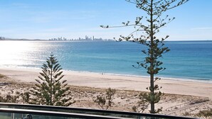 Ein Strand mit freiem Blick auf eine Stadtlandschaft in der Ferne, feinem Sand und spärlicher Vegetation.