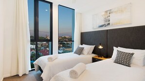 Ein Hotelzimmer mit zwei Betten, einem großen Fenster mit Stadtblick, einem Kopfteil und einer Nachttischlampe.