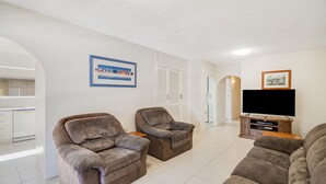 Un salon avec deux fauteuils, un téléviseur à écran plat et un tableau encadré accroché au mur.