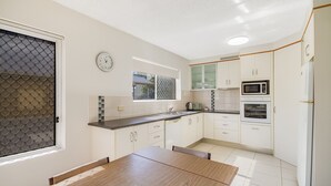 Une cuisine moderne avec des meubles blancs, un four à micro-ondes, un four traditionnel et une table à manger avec des chaises.
