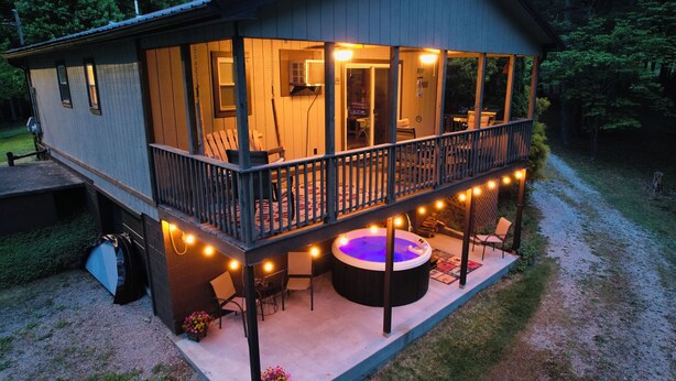 A two-story wooden house with a balcony, a hot tub, and string lights. - HOT TUB COTTAGE near Cave Run Lake, Kentucky, Red River Gorge,Morehead Kentucky (Wellington)