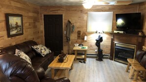 A cozy living room with a brown leather sofa, a wooden coffee table, a fireplace, and a television. - HOT TUB COTTAGE near Cave Run Lake, Kentucky, Red River Gorge,Morehead Kentucky (Wellington)