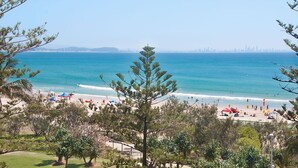 A beach with clear blue water, a sandy shore, and a city skyline in the distance.