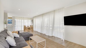 A modern living room with a grey sofa, a wooden coffee table, and a TV mounted on the wall.