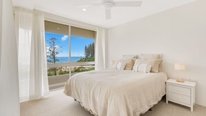 A bedroom with a large window offering a view of the ocean and trees.