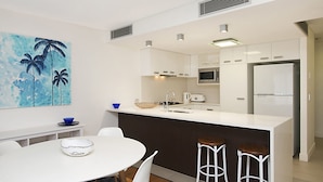 Une cuisine moderne avec des meubles blancs, un îlot central, un four à micro-ondes et un réfrigérateur.