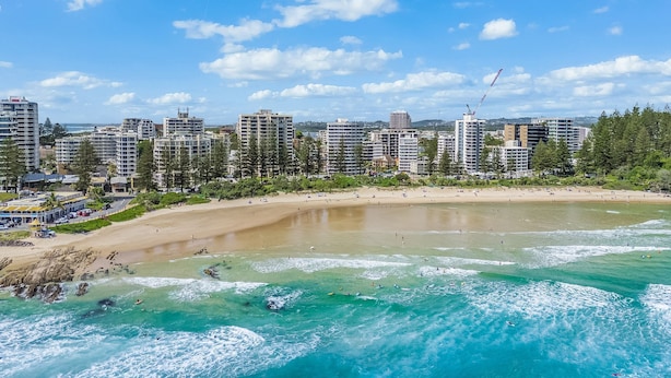 Un paysage urbain côtier avec une plage de sable, des vagues de l’océan et des immeubles de grande hauteur en arrière-plan.