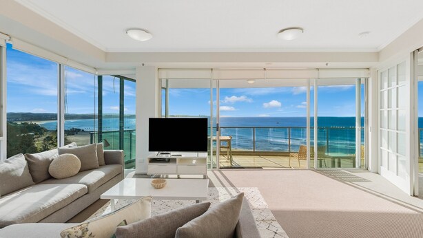 Un salón amplio con televisor grande, asientos cómodos y un balcón con vista al mar.