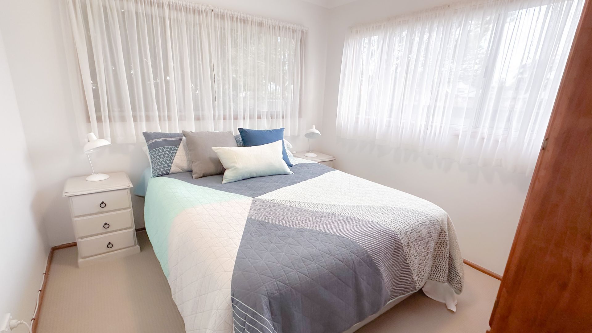 Une chambre à coucher avec un lit, deux tables de chevet, une commode et des rideaux légers.