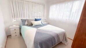 Ein Schlafzimmer mit einem Bett, zwei Nachttischen, Vorhängen und durchsichtigen Gardinen.