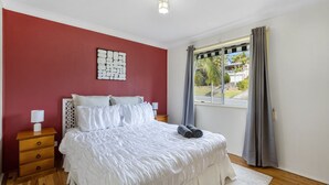 Une chambre à coucher avec un lit, une table de chevet, une lampe, une fenêtre avec des rideaux et une vue sur l’extérieur.