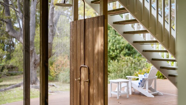 Une porte en bois avec une poignée en laiton, un escalier avec des rampes blanches et une terrasse aménagée avec du mobilier d’extérieur.