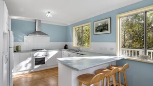 Une cuisine moderne avec des armoires blanches, un four encastré, une cuisinière à gaz et une grande fenêtre donnant sur la verdure.