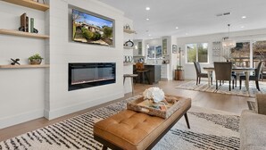 A modern living room with a fireplace, a television mounted on the wall, and a dining area with a chandelier. - Urban Elegance in Wine Country: Unwind Just Steps from Healdsburg Plaza! (Healdsburg)