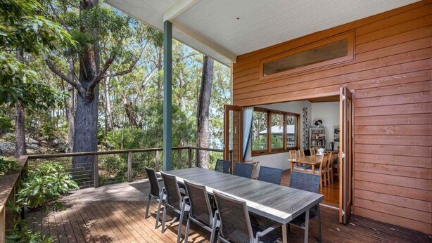 Une terrasse en bois avec une table et des chaises, entourée d’arbres.