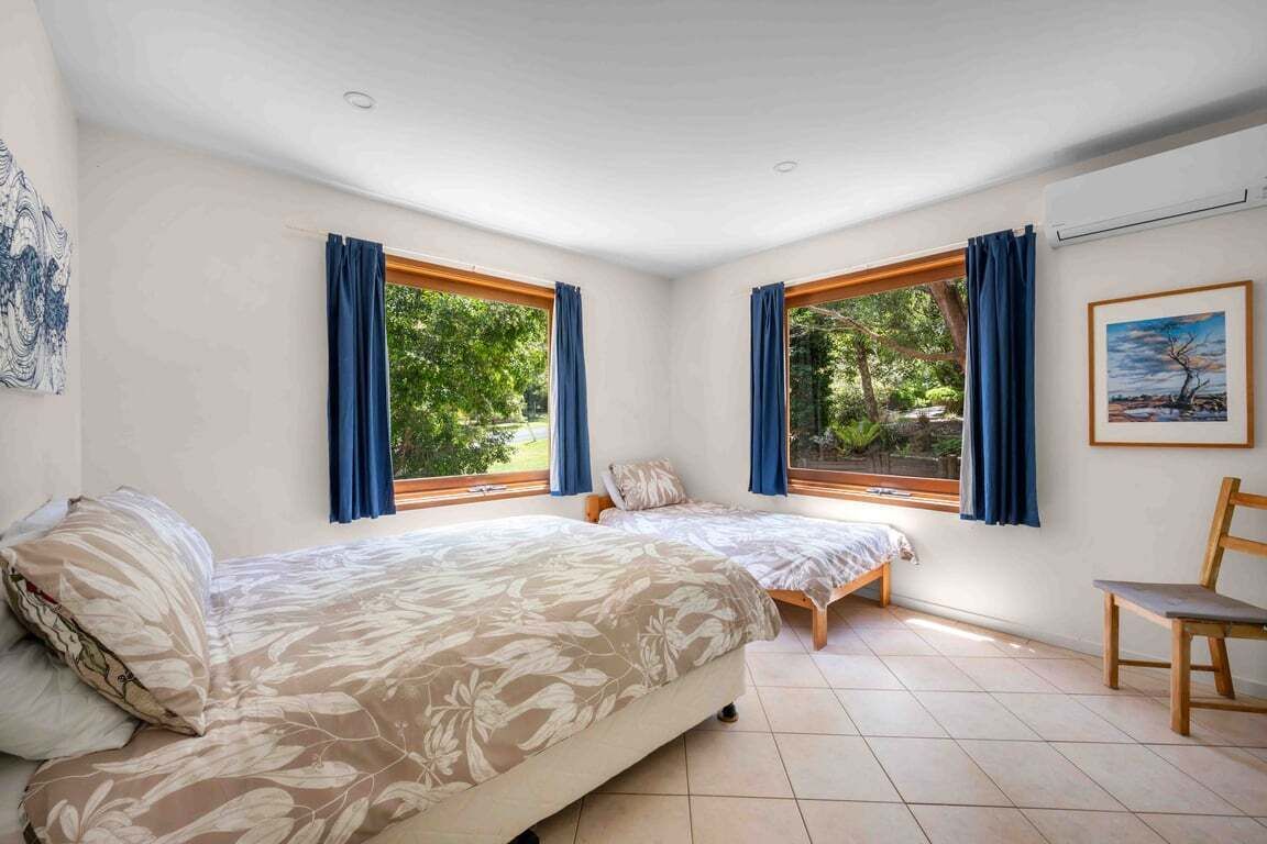 A bedroom with two beds, large windows, and a view of greenery.