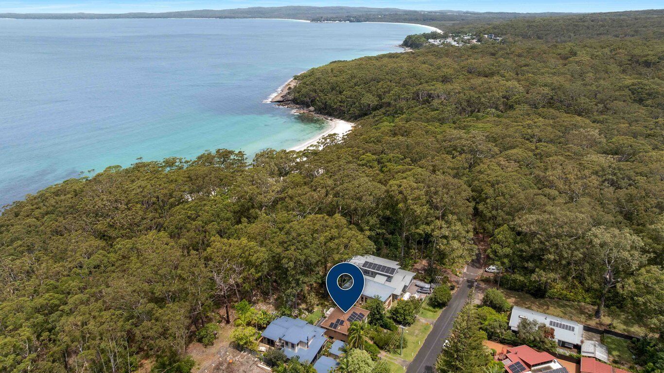 Eine Luftaufnahme einer Küstenimmobilie mit dichtem Wald, einem Strand und einem Haus mit Solaranlage.