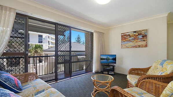 A balcony with a sliding glass door, wicker furniture, a television, and a painting on the wall.