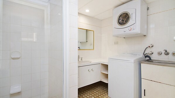 Une salle de bain moderne équipée d’une douche, d’un lavabo, d’un miroir et d’un lave-linge.