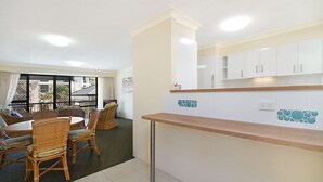 Une chambre d’hôtel compacte dotée d’une kitchenette, d’un coin repas avec des meubles en osier et d’un balcon offrant une vue sur les bâtiments environnants.