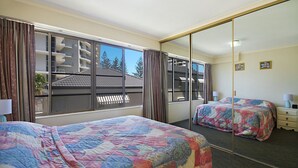 Une chambre d’hôtel avec deux lits, un grand miroir et une vue sur un immeuble doté d’un balcon.