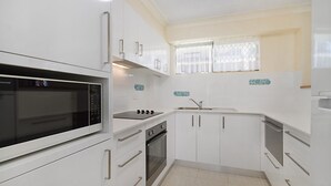 Une cuisine de taille réduite avec des meubles blancs, un four à micro-ondes, une cuisinière et un évier.