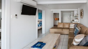 Un salon moderne avec un canapé beige, une table basse et un téléviseur à écran plat fixé au mur.
