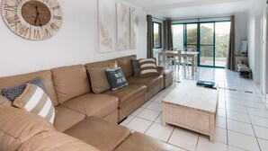 Un salon moderne avec un canapé beige, une table basse en bois et une grande fenêtre donnant sur un paysage verdoyant.