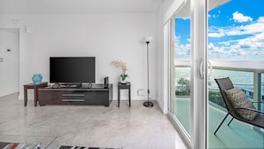 A modern living room with a flat-screen TV, a dark wooden entertainment unit, a small side table with a vase, and a floor lamp. - Apartment Luxury The Tides on the Beach with Ocean View  (Hollywood)